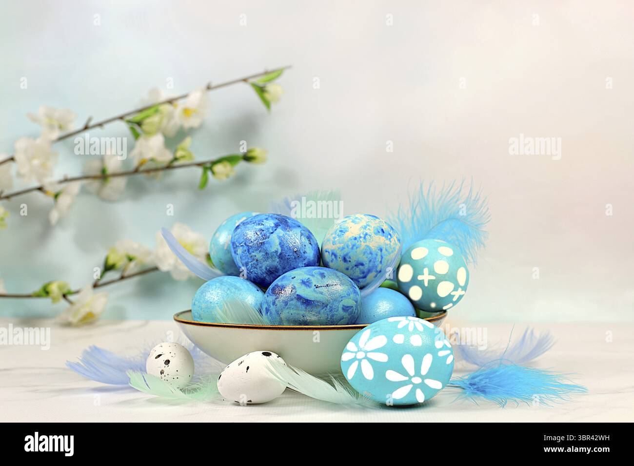 Happy Easter-Konzept. Abstrakte Osterkomposition mit blau verzierten Eiern, Federn, blühenden Zweigen und Blumen. Banner für Bildschirm mit Platz für Stockfoto