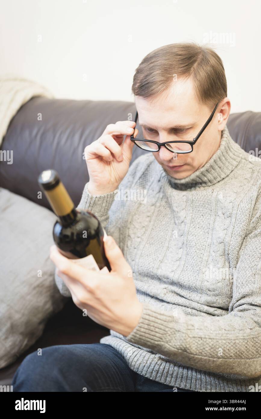 Mann hält eine Rotwein-Flasche in der Hand und plant, sich zu Hause zu entspannen Stockfoto