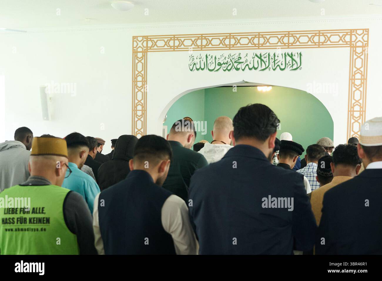 6. Juni 2025, Berlin: Muslimische Männer beten in der Khadija-Moschee für das muslimische fest von Eid al-Adha. Das islamische Glaubensbekenntnis steht in Arabisch über der Gebetsnische. Der so genannte Shah·da gilt als eine der fünf Säulen des Islam und ist für fromme Muslime von zentraler Bedeutung. Foto: Annette Riedl/dpa Stockfoto