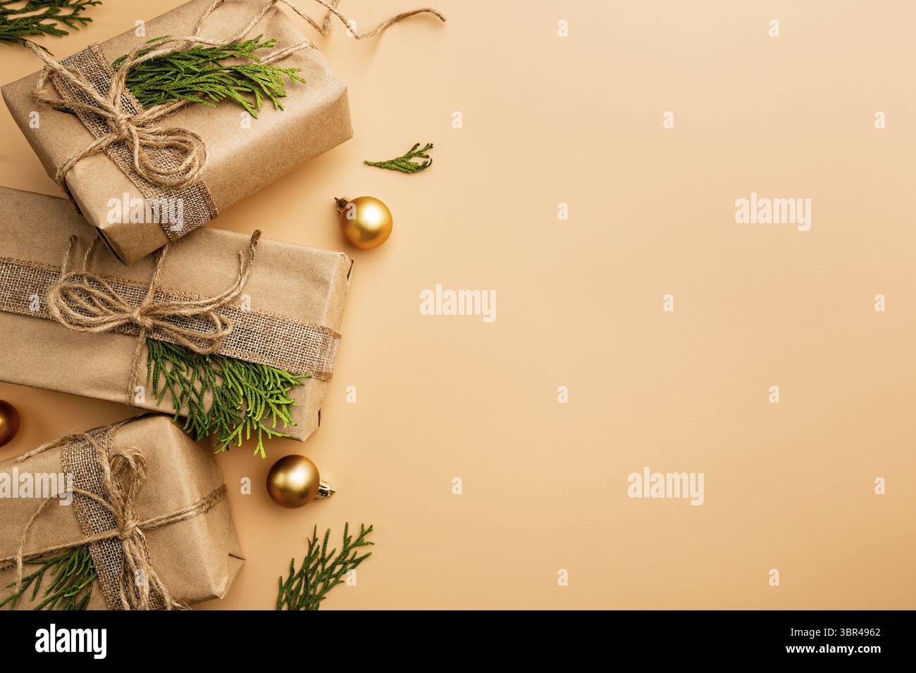 Weihnachtsgeschenk oder Geschenkschachtel in Kraftpapier mit Dekoration auf Gold oder Champagner Hintergrund verpackt, Draufsicht mit Kopierraum Stockfoto