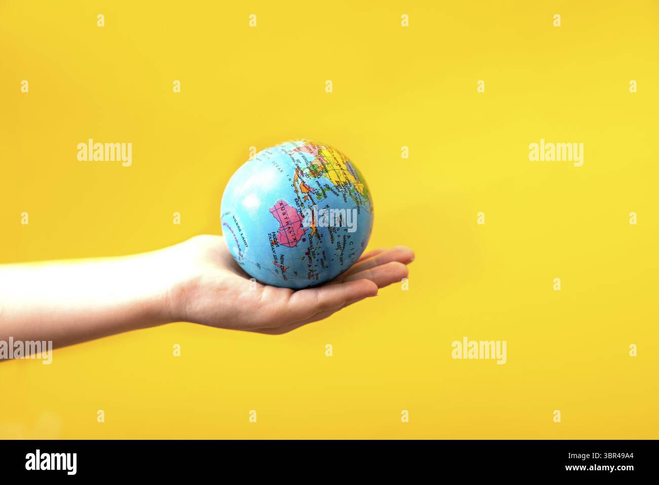 Gütiger Handhaelt Globus in einer Hand auf gelbem Hintergrund. Welttag der Erde Konzept. Gruene Energie, erneuerbare und nachhaltige Ressourcen. Schuetz Stockfoto