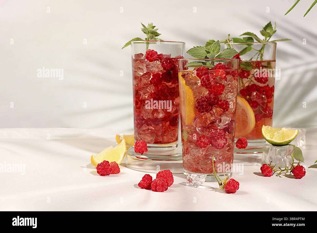 Entgiftungswasser mit Fruchtgeschmack auf hellem Hintergrund. Erfrischender hausgemachter Limonade-Cocktail im Sommer, Mojito mit Himbeeren, Johannisbeeren, Minze und Zitrone, Stockfoto