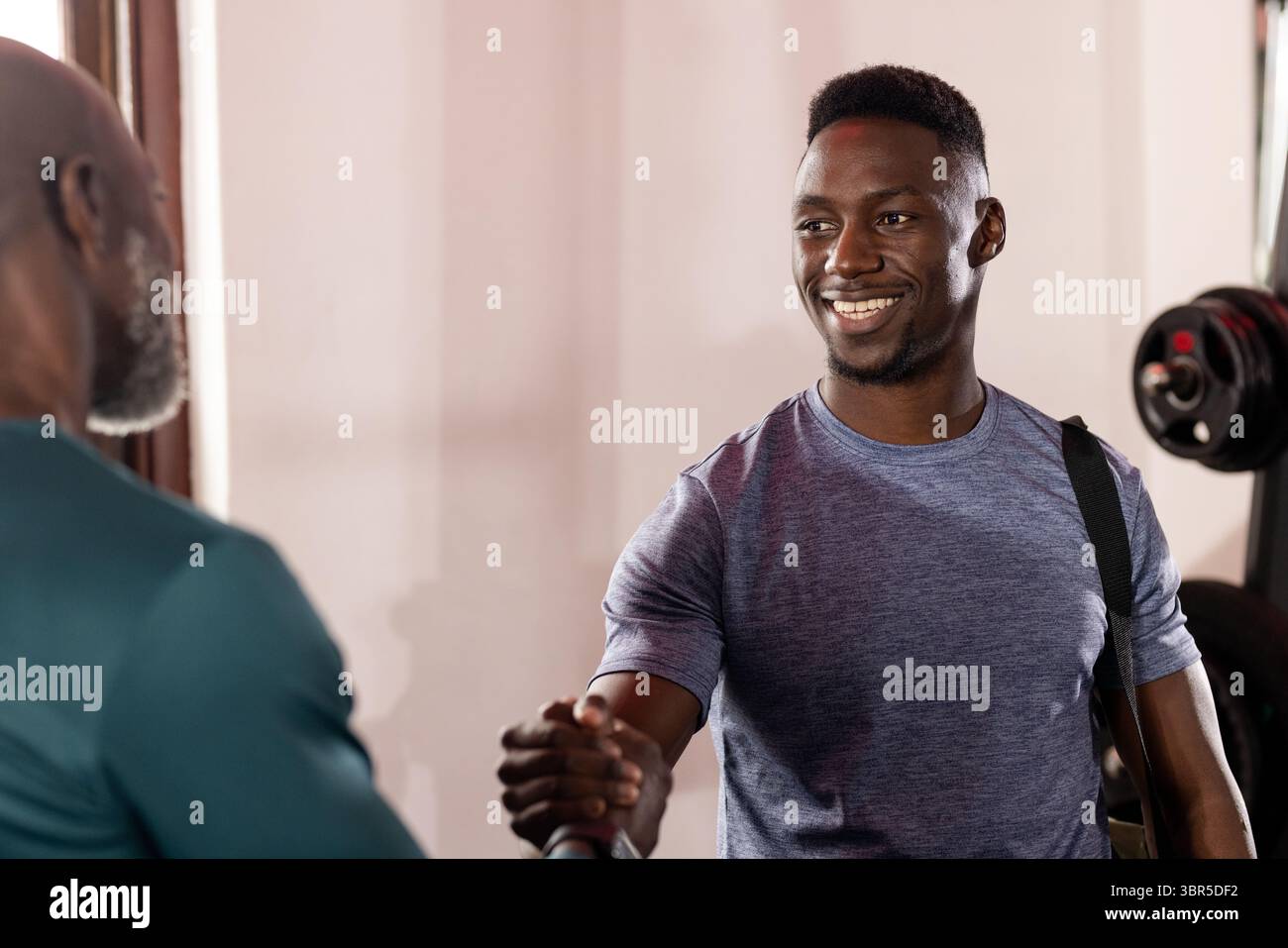 Afrikanisch-amerikanischer Trainer und Kunde schütteln sich die Hände im Fitnessbereich, während sie den Trageriemen tragen Stockfoto