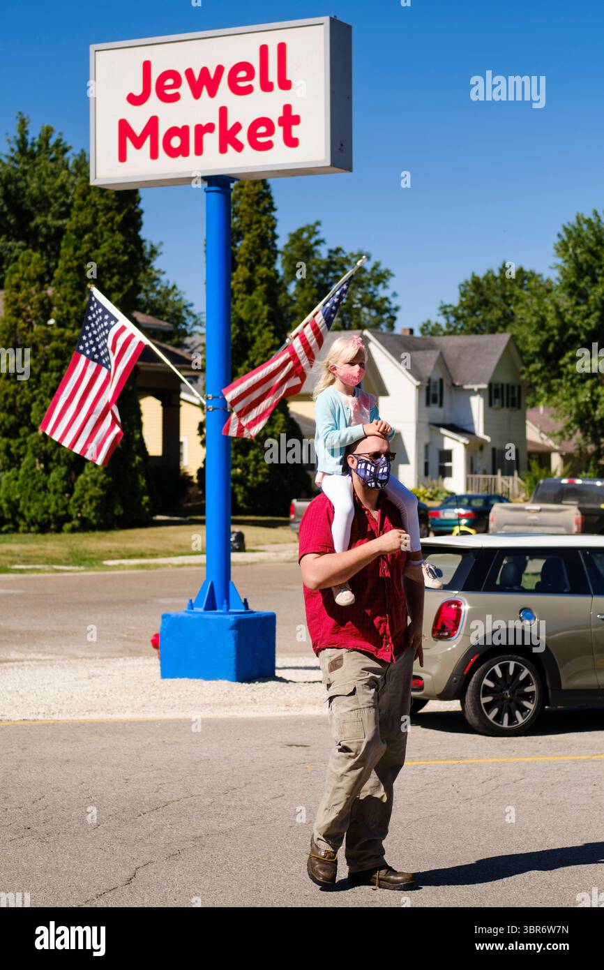 3. August 2020, Jewell, Iowa, USA: Ein Mann mit seiner Tochter auf den Schultern geht zum Jewell Market. Der einzige Supermarkt in Jewell, einer kleinen Gemeinde im Zentrum von Iowa, wurde 2019 geschlossen. Es diente vier Gemeinden im Umkreis von 20 Meilen um Jewell. Einige Bewohner der Stadt gründeten eine Genossenschaft, um den Laden wieder zu eröffnen. Sie verkauften Aktien an die Co-op und hielten Spendenaktionen im Frühjahr ab. Die Organisatoren sammelten etwa 225.000 US-Dollar und kauften den Laden, der am 8. Juli seine „weiche Öffnung“ hatte. Der Laden feierte seine offizielle Wiedereröffnung am 3. August. Vor der Wiedereröffnung war Jewell ein „Food des“ gewesen Stockfoto