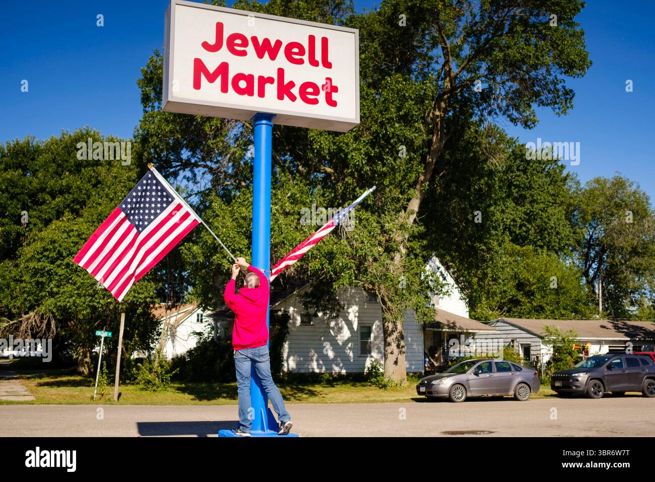 August 2020, Jewell, Iowa, USA: GARREN ZANKER, manager des Jewell Market, passt die amerikanischen Flaggen auf dem Schild vor dem Laden an. Der einzige Supermarkt in Jewell, einer kleinen Gemeinde im Zentrum von Iowa, wurde 2019 geschlossen. Es diente vier Gemeinden im Umkreis von 20 Meilen um Jewell. Einige Bewohner der Stadt gründeten eine Genossenschaft, um den Laden wieder zu eröffnen. Sie verkauften Aktien an die Co-op und hielten Spendenaktionen im Frühjahr ab. Die Organisatoren sammelten etwa 225.000 US-Dollar und kauften den Laden, der am 8. Juli seine „weiche Öffnung“ hatte. Der Laden feierte seine offizielle Wiedereröffnung am 3. August. Vor dem r Stockfoto