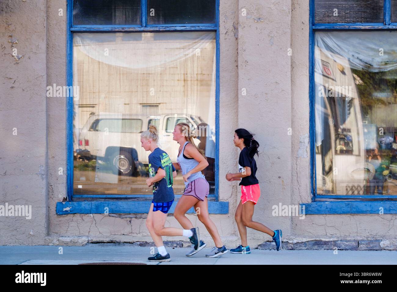 3. August 2020, Jewell, Iowa, USA: Mädchen joggen entlang der Main Street in Jewell Monday. Der einzige Supermarkt in Jewell, einer kleinen Gemeinde im Zentrum von Iowa, wurde 2019 geschlossen. Es diente vier Gemeinden im Umkreis von 20 Meilen um Jewell. Einige Bewohner der Stadt gründeten eine Genossenschaft, um den Laden wieder zu eröffnen. Sie verkauften Aktien an die Co-op und hielten Spendenaktionen im Frühjahr ab. Die Organisatoren sammelten etwa 225.000 US-Dollar und kauften den Laden, der am 8. Juli seine „weiche Öffnung“ hatte. Der Laden feierte seine offizielle Wiedereröffnung am 3. August. Vor der Wiedereröffnung war Jewell sieben Monate lang eine „Essenswüste“. Stockfoto