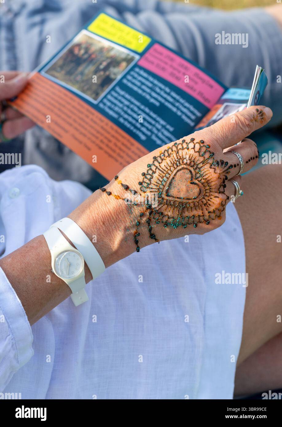 Eine Frau mit einem Herzen entwirft Henna Körperkunst auf ihrer Handfläche, während sie ein kleines Heft liest. Stockfoto