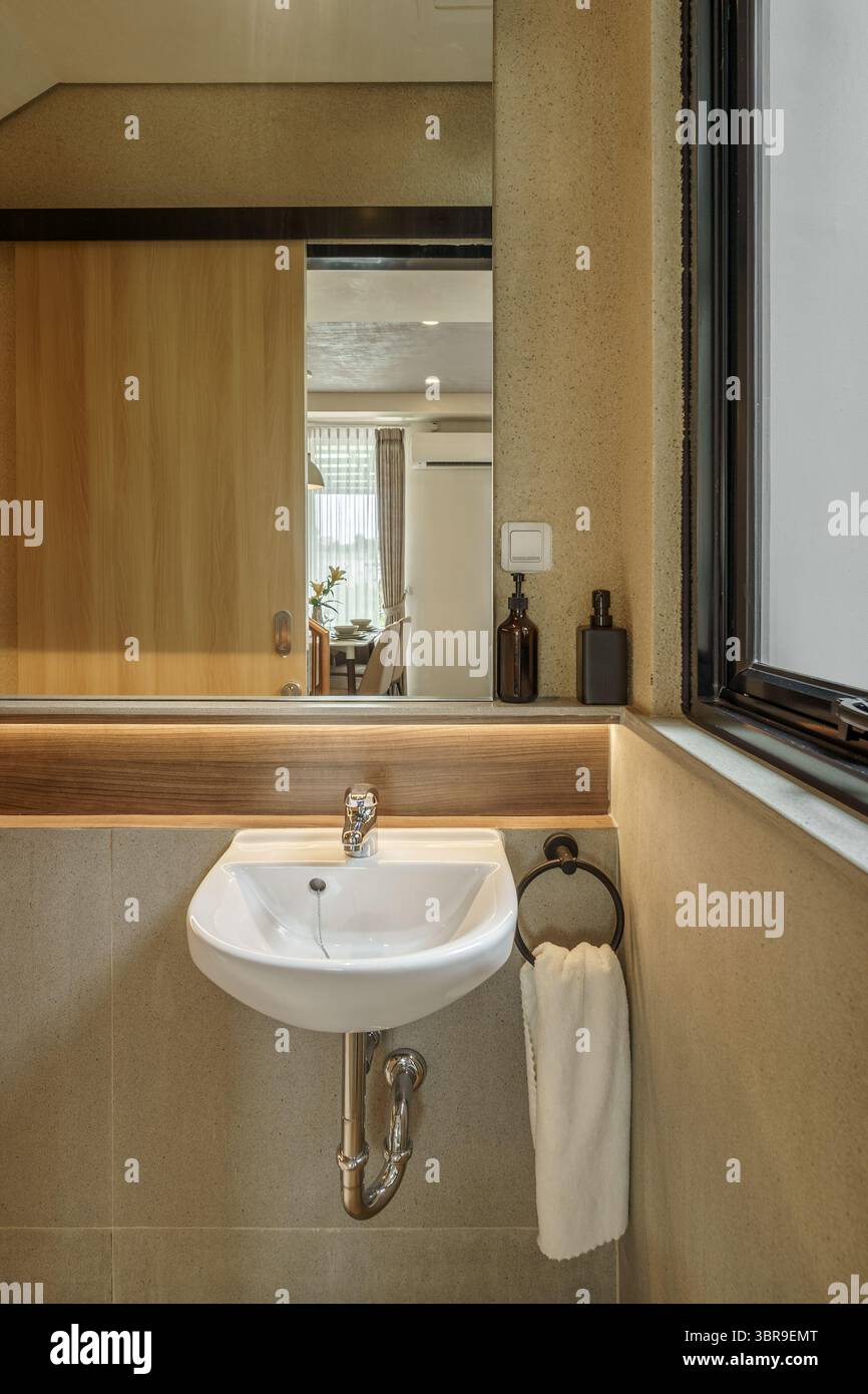 Titel: Modernes Badezimmer mit Wandwaschbecken, warmer Beleuchtung unter dem Spiegel und Spiegel im Essbereich. Saubere, minimalistische Innenausstattung im Japandi-Stil Stockfoto