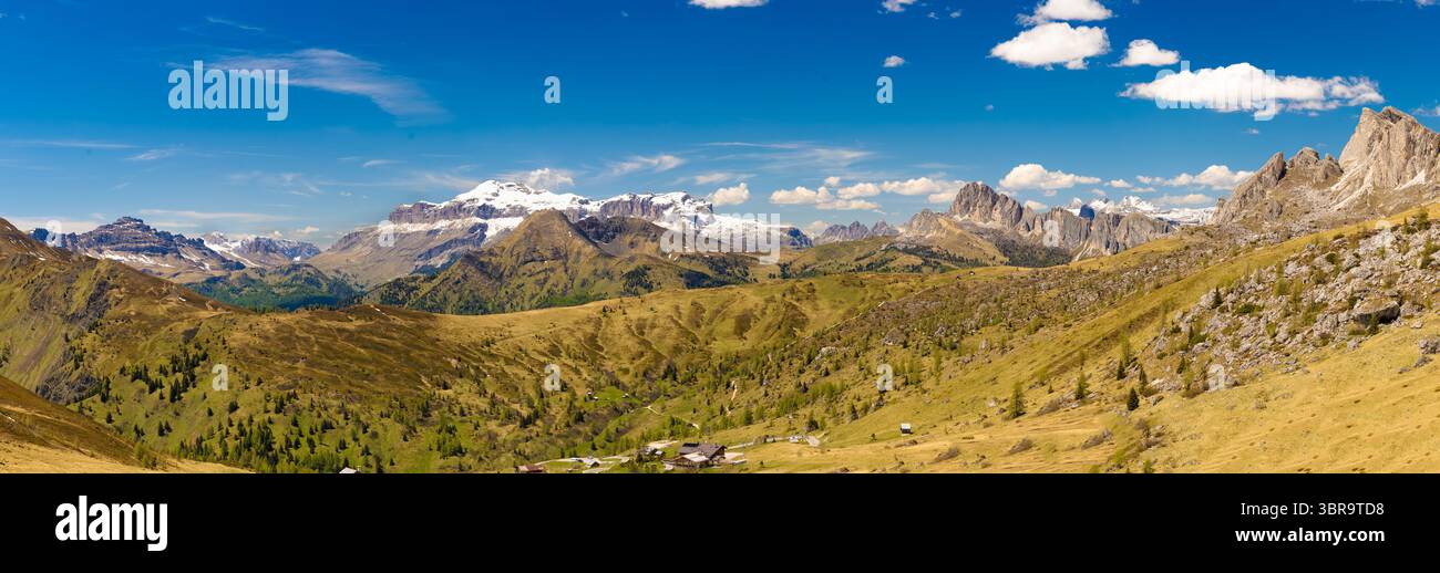 Panoramic view of Monte Civetta and Col di Lana from Passo di Giau, showcasing snow-capped peaks, rolling green slopes, and scattered houses under a v Stockfoto