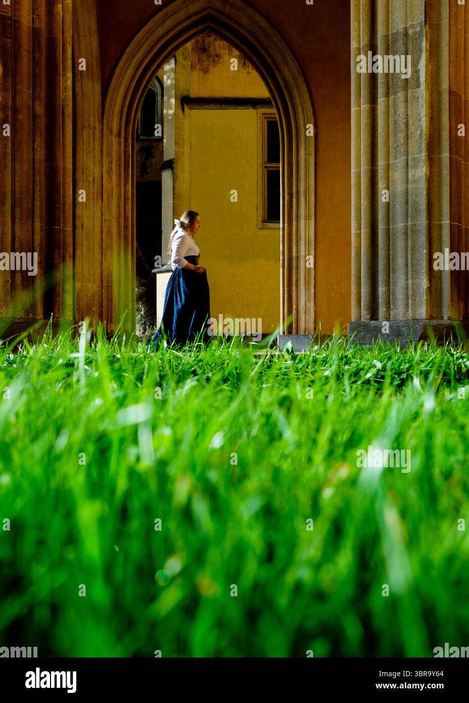 Eine Frau in historischem Kleid steht in einem Bogen, mit grünem Gras im Vordergrund. Stockfoto