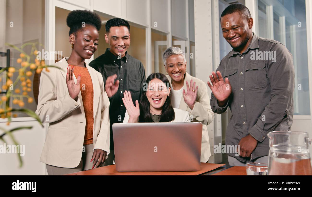 Gruppe von Kollegen lächelt und winkt während eines virtuellen Business Meetings in einem modernen Büro Stockfoto