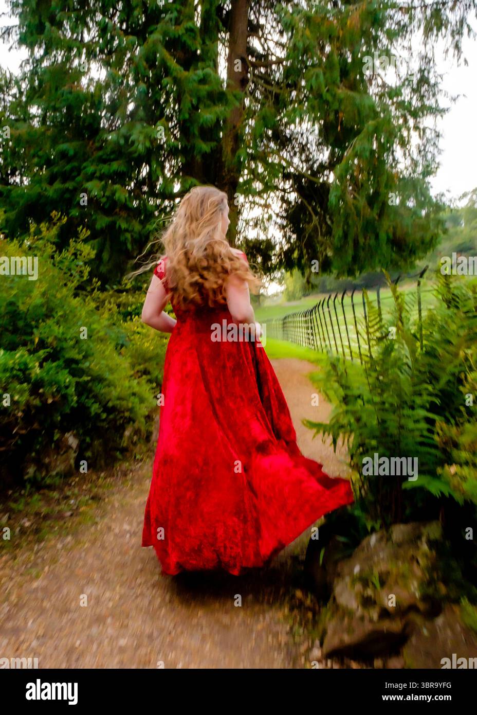 Eine Frau in rotem Kleid läuft einen Weg in einem Park entlang. Stockfoto