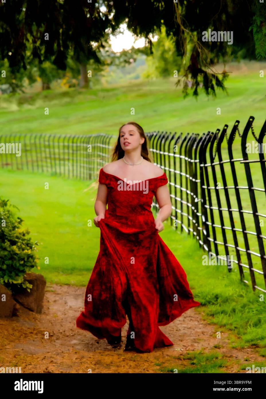 Eine Frau in rotem Kleid läuft auf einem Weg in einem Park. Stockfoto