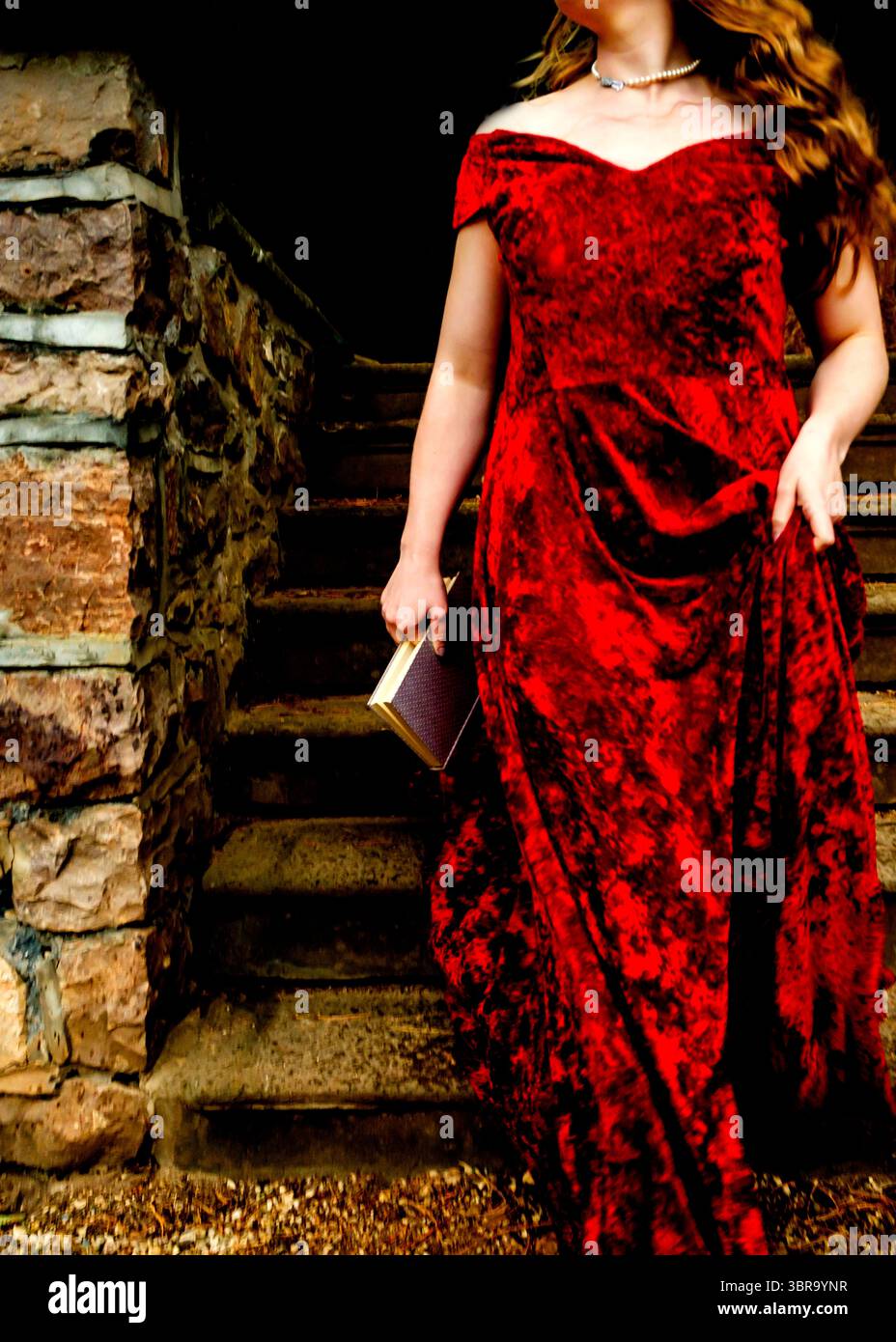 Eine Frau in rotem Kleid steigt eine Steintreppe hinab und hält ein Buch. Stockfoto