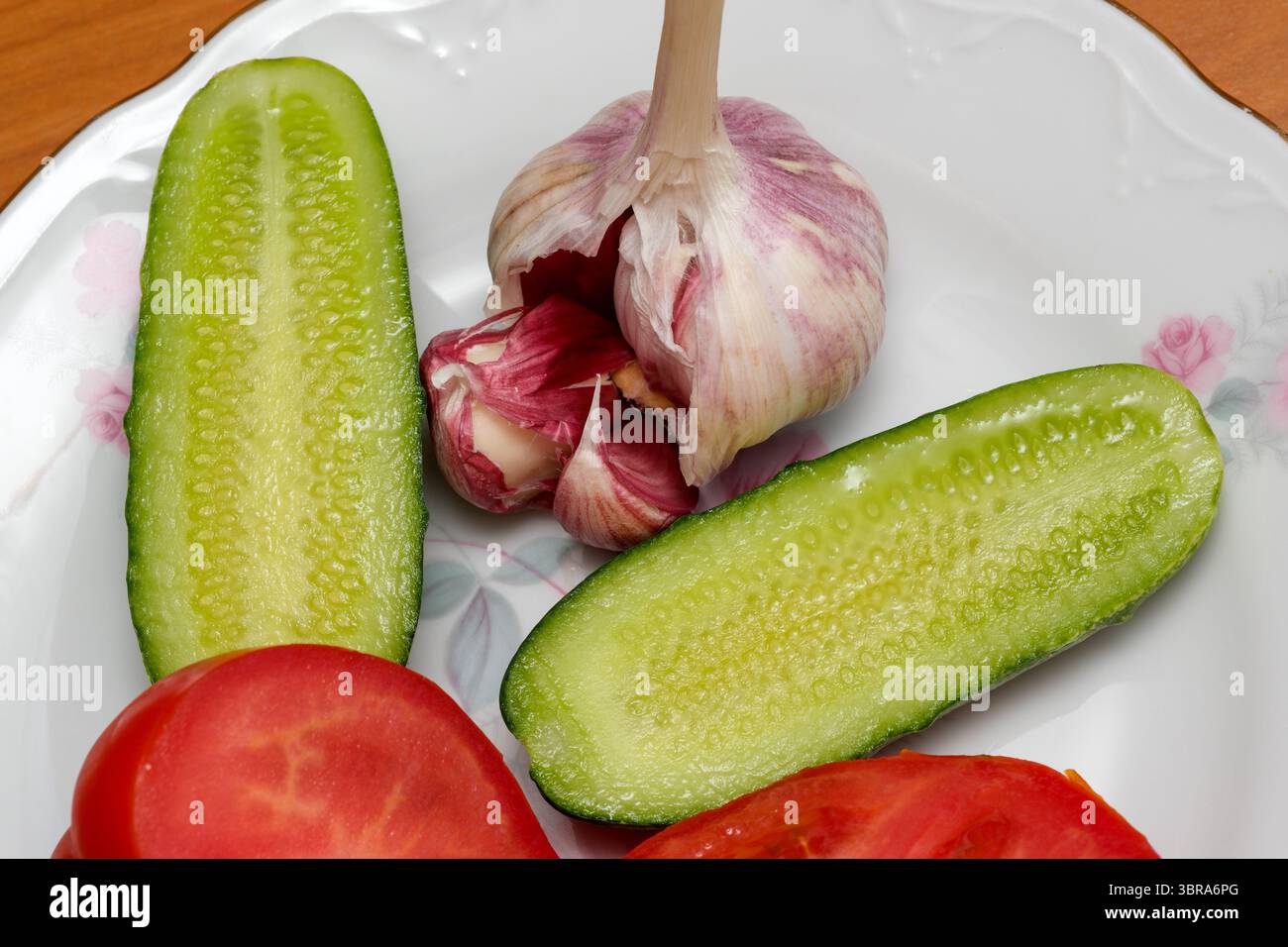 Gurkenscheiben, reife Tomaten und ganze Knoblauchzehen warten auf die Zubereitung. Stockfoto
