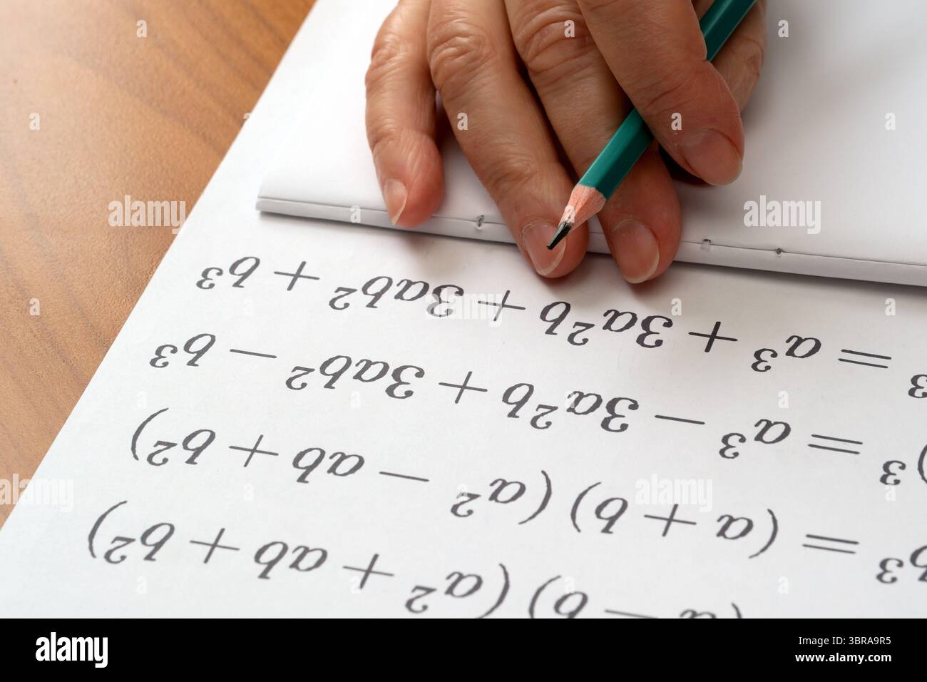 Eine Hand schreibt sorgfältig mathematische Gleichungen auf einen Notizblock an einem hölzernen Schreibtisch. Stockfoto