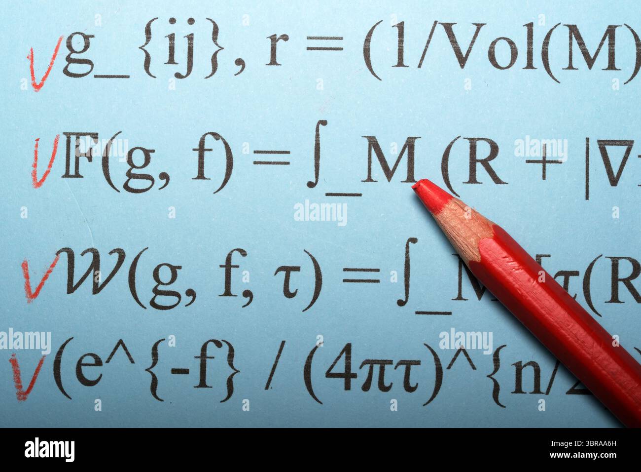 Ein Schüler hebt Gleichungen hervor, die in Rot und Schwarz auf einem blauen Blatt Papier geschrieben sind. Stockfoto