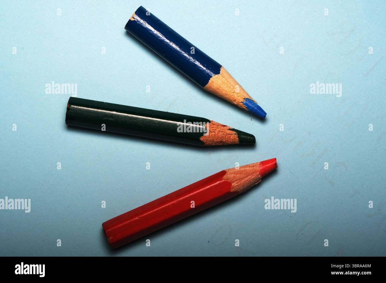 Drei bunte Bleistifte ruhen auf einer beruhigenden blauen Oberfläche und sind bereit für kreativen Ausdruck. Stockfoto