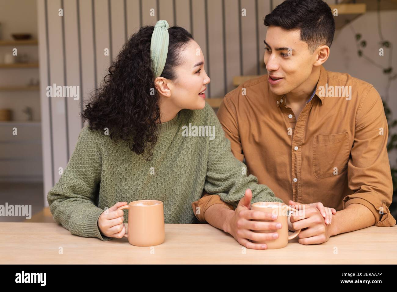 Verschiedene Paare sitzen am Holztisch und halten Keramikbecher und plaudern im Essbereich Stockfoto