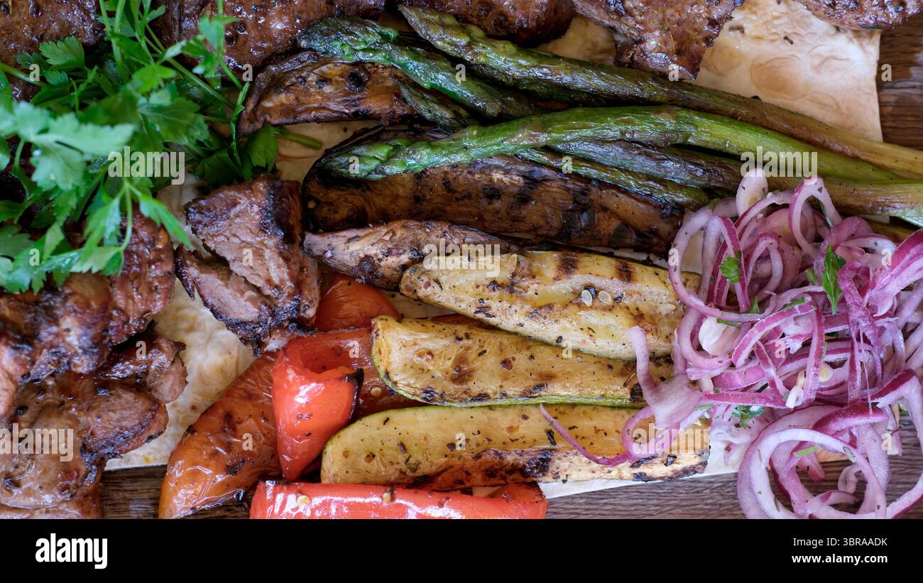 Eine verlockende Auswahl an gegrilltem Fleisch und frischem Gemüse, garniert mit Kräutern. Stockfoto