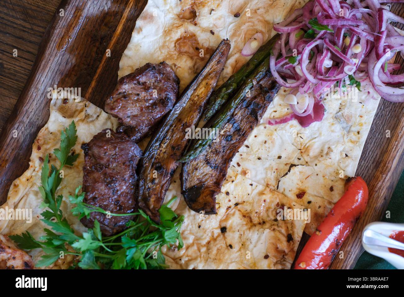 Herzhaftes Grillfleisch und frisches Gemüse auf warmem Fladenbrot mit Kräutern. Stockfoto