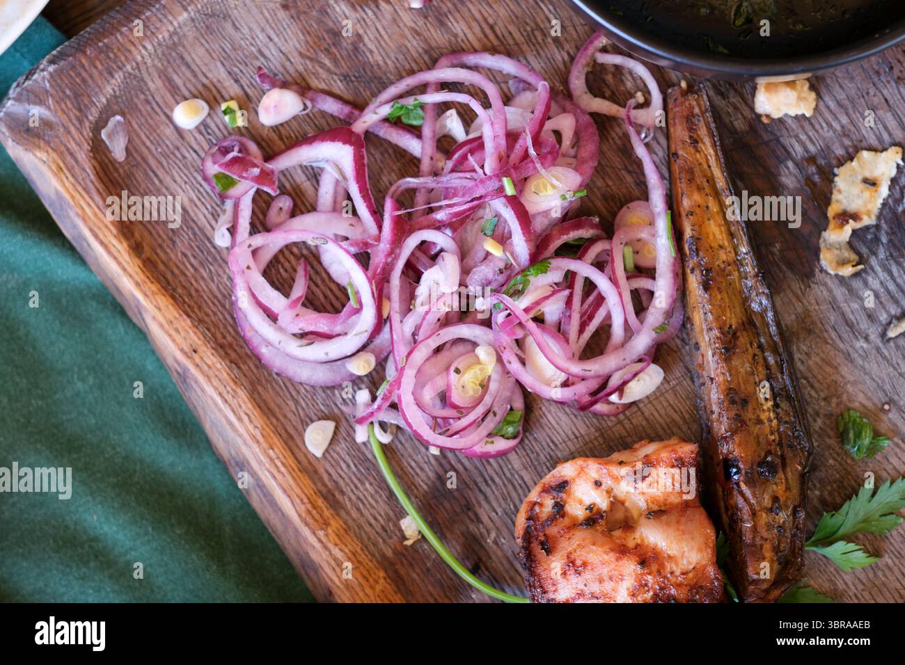 Saftiges gegrilltes Hühnchen, frische Kräuter und würzige Zwiebeln sorgen für ein fest auf einem rustikalen Brett. Stockfoto