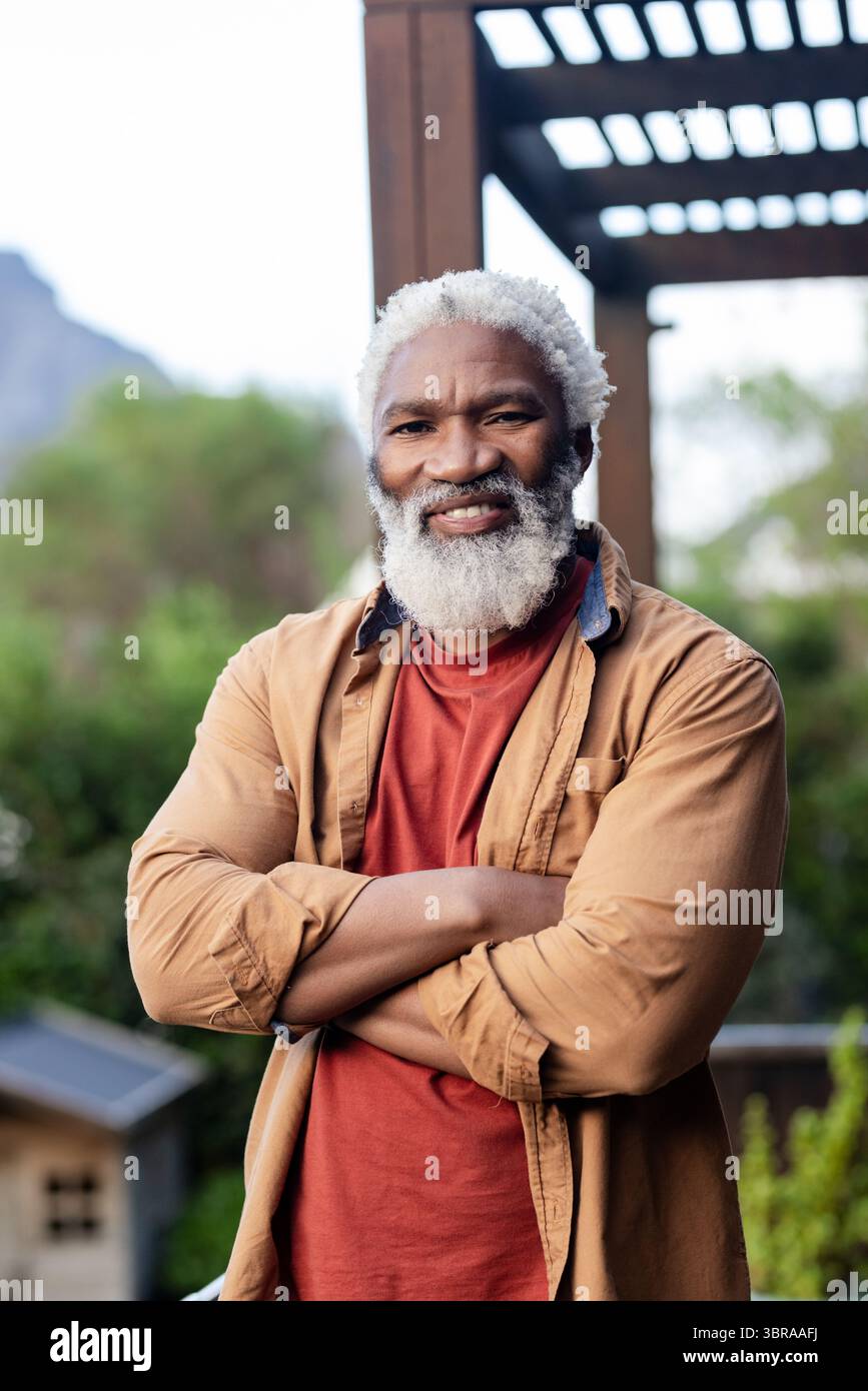 Afroamerikaner Senior Mann, der unter hölzernen Pergolen auf der Terrasse des Hinterhofs steht und lässige Hemden trägt Stockfoto