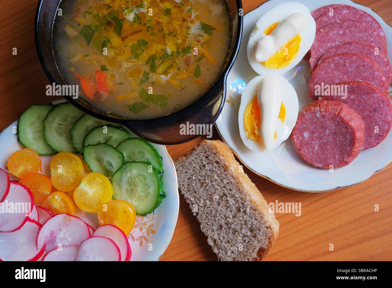 Eine herzhafte Schüssel Suppe umgeben von gekochten Eiern, Fleischscheiben und farbenfrohem Gemüse Stockfoto
