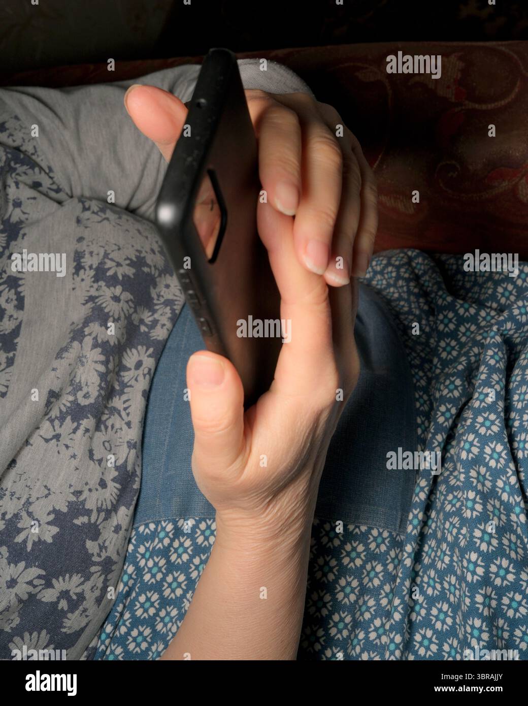 Eine Person sitzt bequem im Bett und ist spät in der Nacht mit ihrem Smartphone beschäftigt. Stockfoto