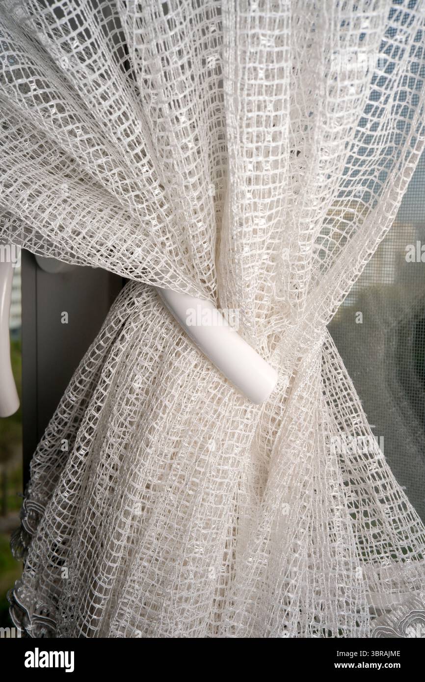 Der zarte weiße Vorhang schwingt leicht durch ein offenes Fenster und lädt zur frischen Luft ein. Stockfoto