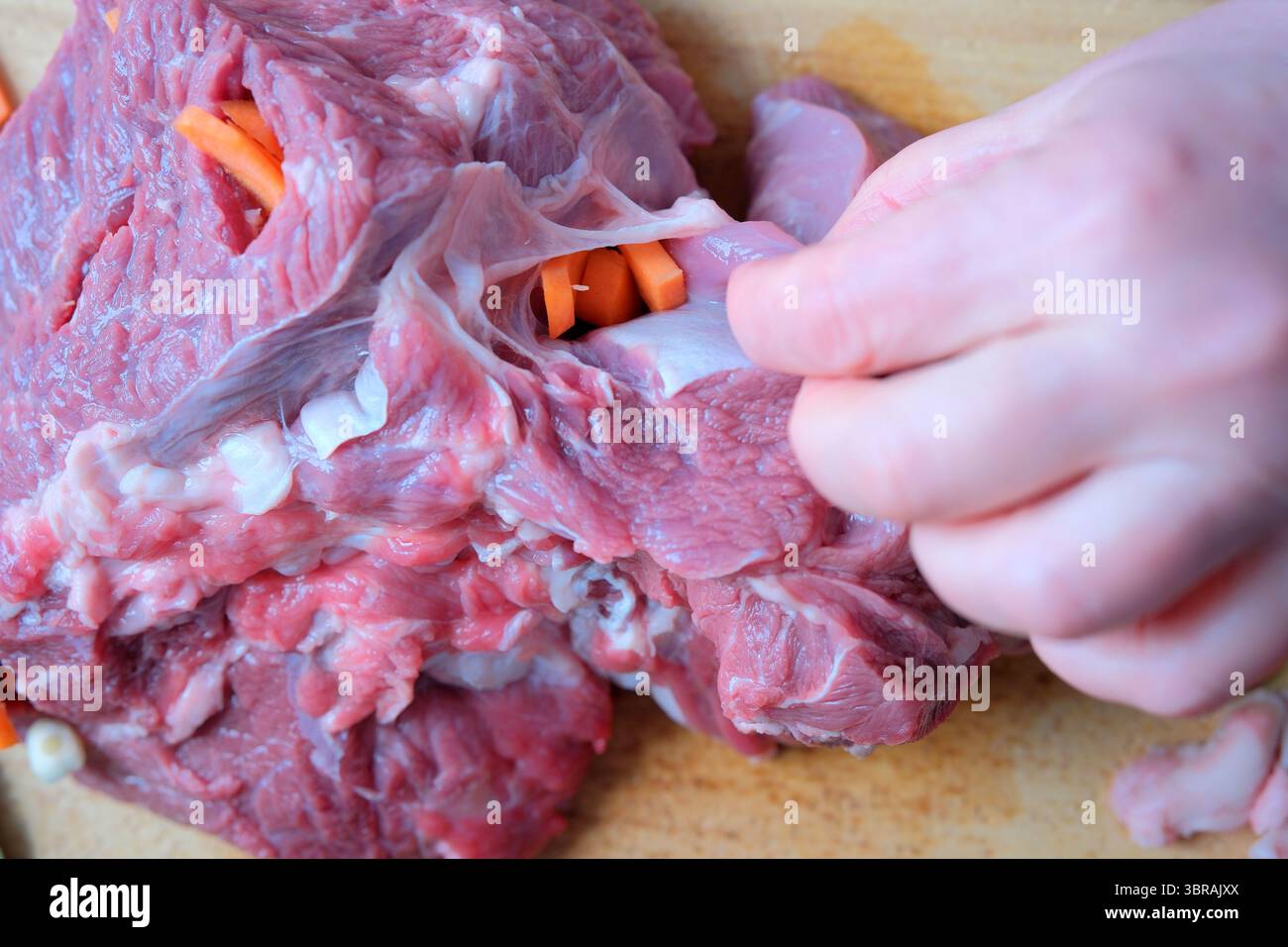Geschickte Hände füllen frisches Gemüse in einen Fleischschnitt auf einem Holzbrett. Stockfoto