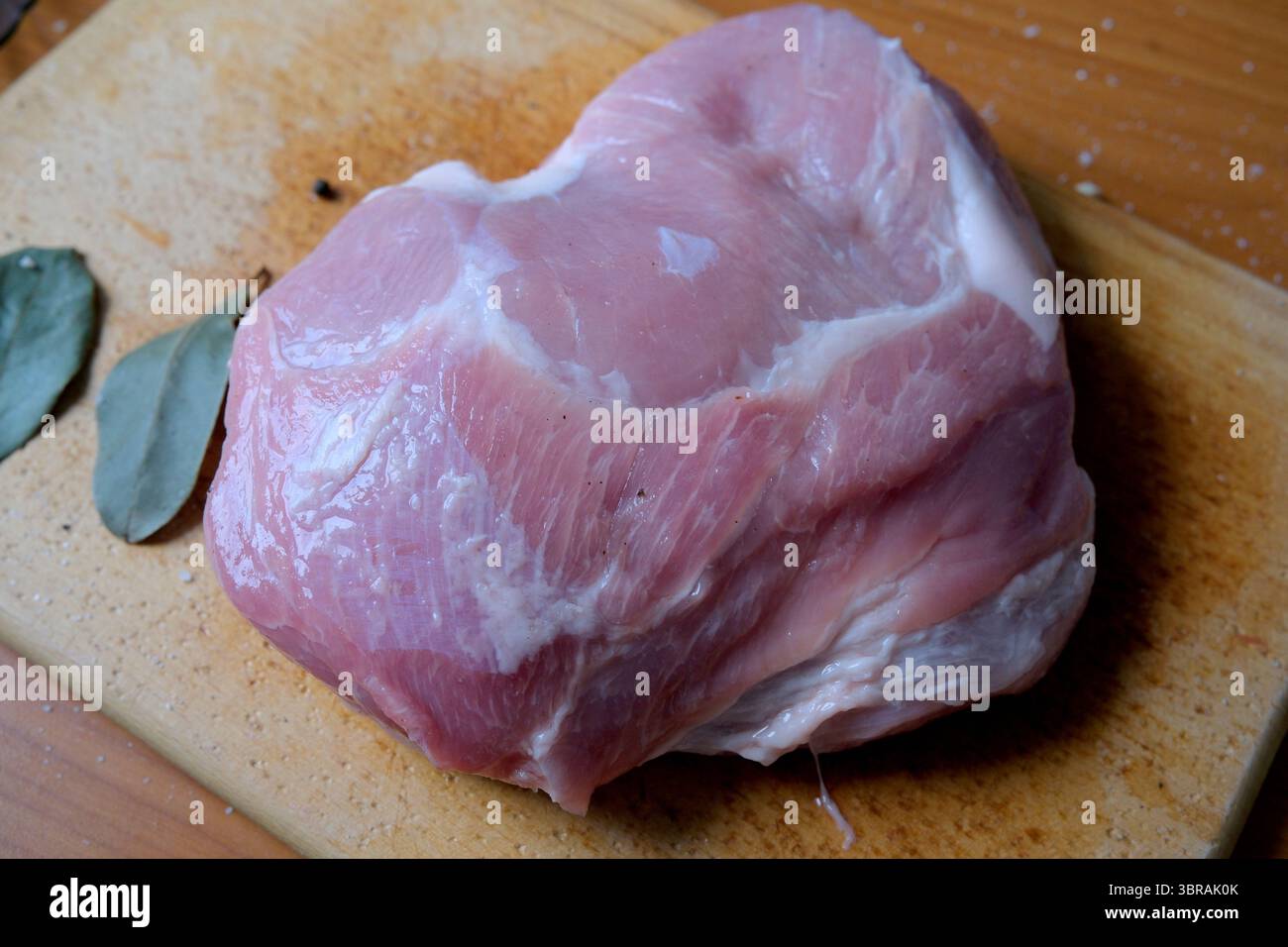 Ein Schweinefleisch auf einem Holzbrett mit Lorbeerblättern, fertig zum Kochen. Stockfoto