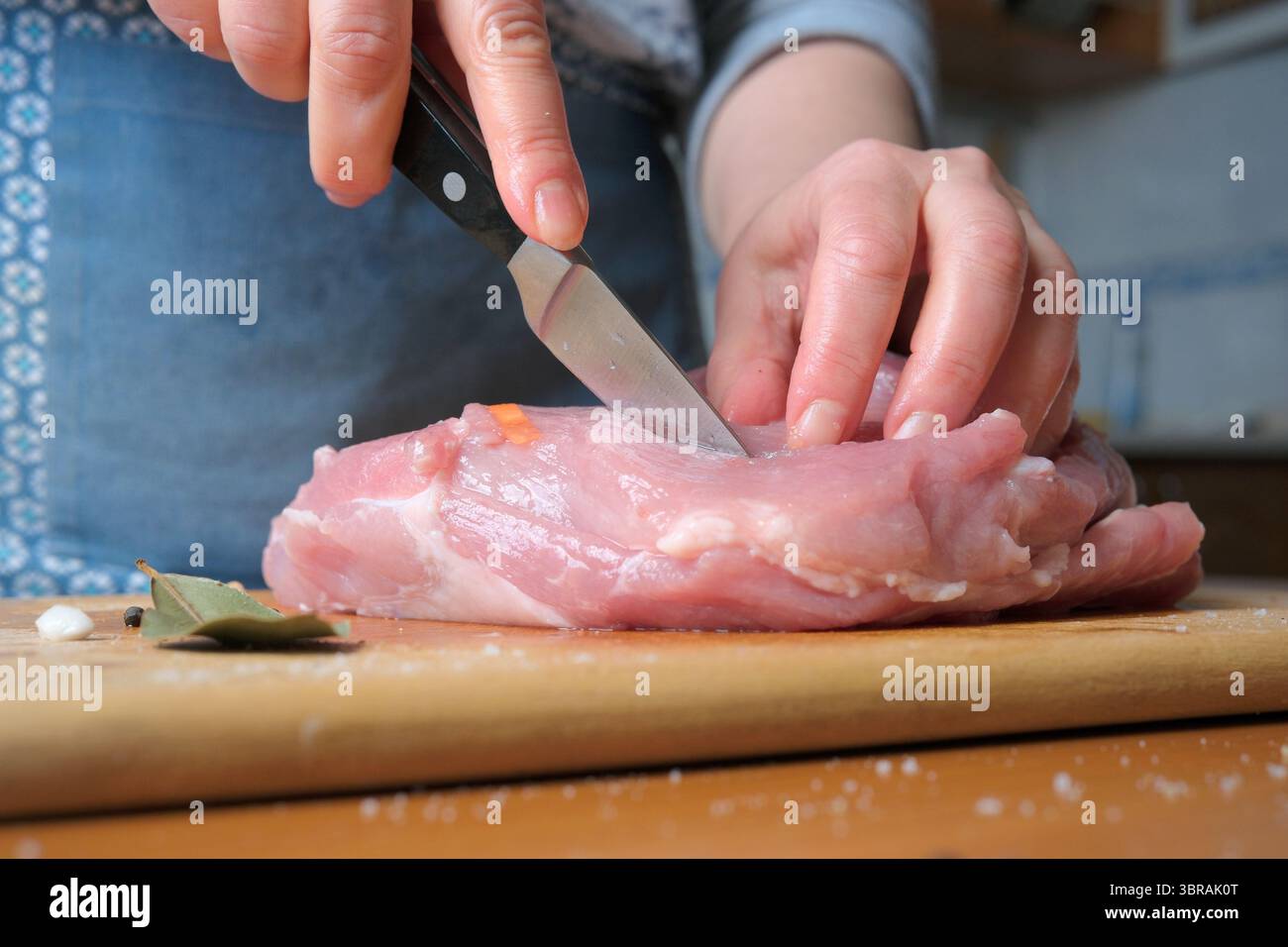 In einer gemütlichen Küche schneiden Sie das Schweinefleisch mit den Händen auf einem hölzernen Schneidebrett. Stockfoto