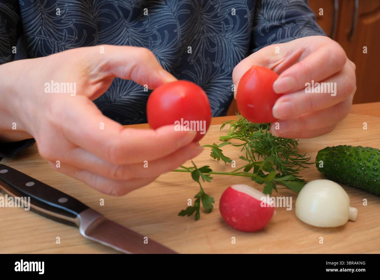 Hände halten reife Tomaten vorsichtig, während frische Kräuter und Gemüse umgeben sind. Stockfoto