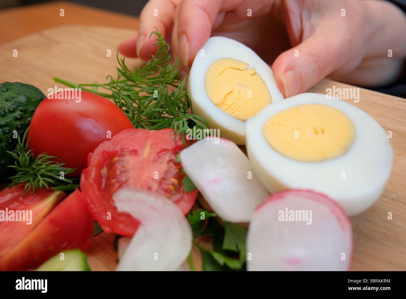 Gemüse und gekochte Eier auf einem Holzbrett für ein gesundes Gericht hacken. Stockfoto