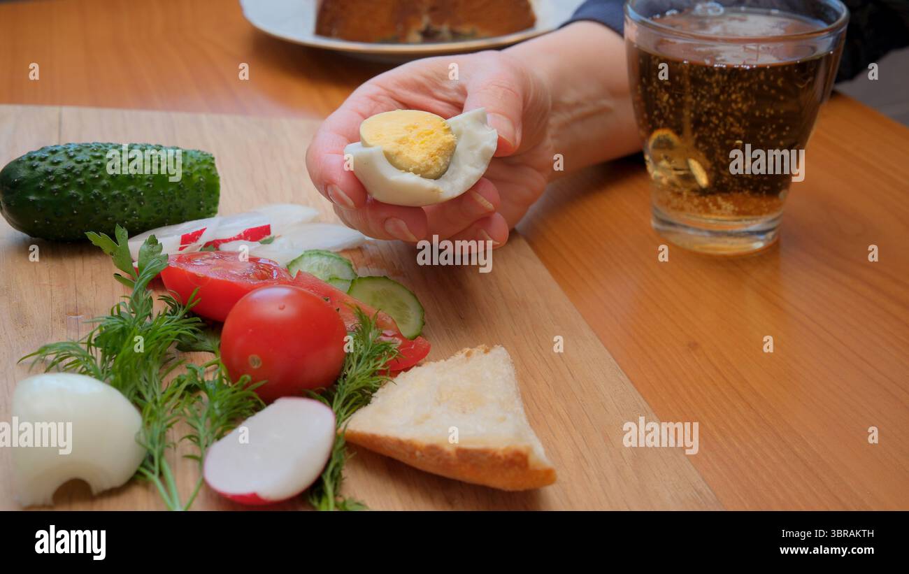 Eine Hand hält ein gefülltes Ei neben lebendigem Gemüse auf einem Holztisch. Stockfoto