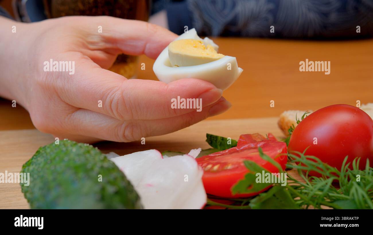 Eine Hand präsentiert ein weich gekochtes Ei neben frischem Gemüse und Kräutern. Stockfoto
