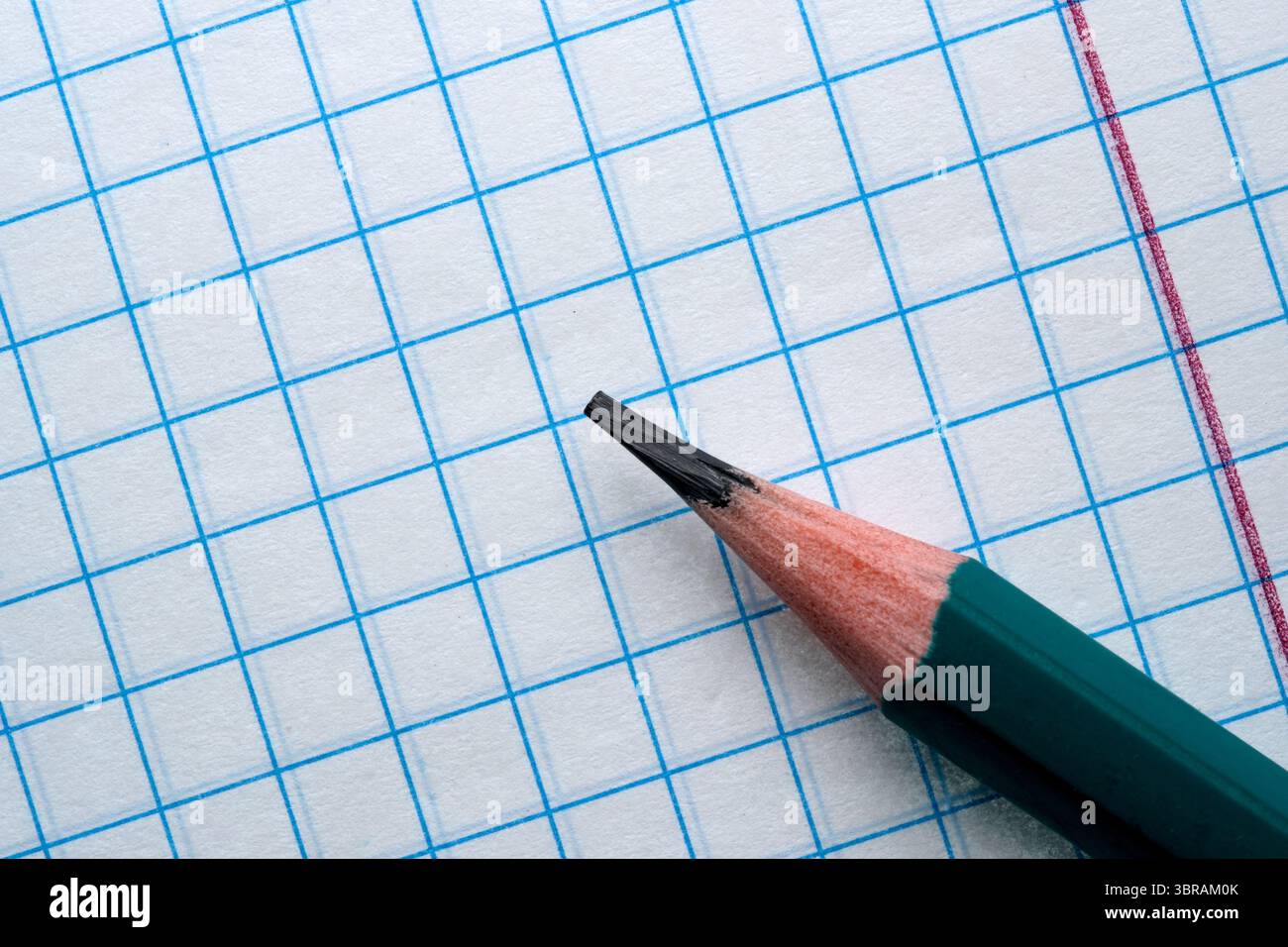 Ein geschärfter Bleistift liegt direkt über einem Gitterpapier auf, bereit für die Arbeit. Stockfoto