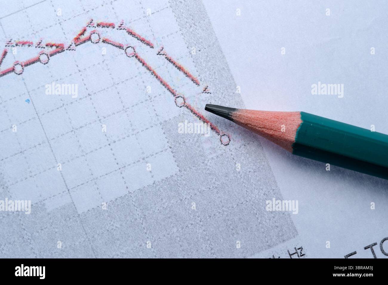 Ein farbiger Bleistift steht auf einer Grafik mit rückläufigen Finanztrends. Stockfoto