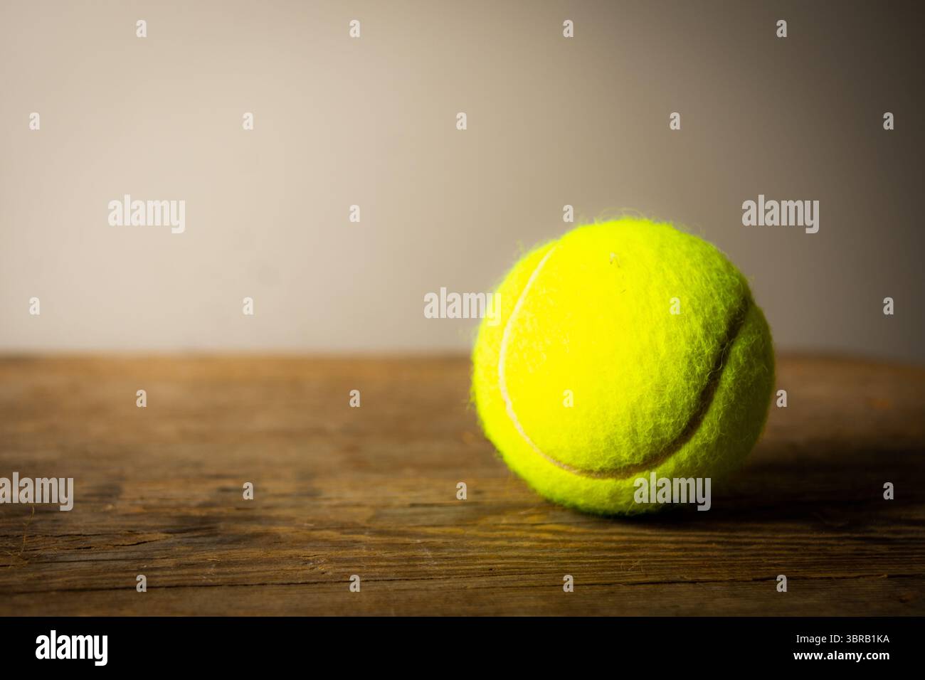 Hellgelber Tennisball auf einem rustikalen Holztisch vor einem neutralen, graduierten Hintergrund mit viel Kopierraum. Stockfoto