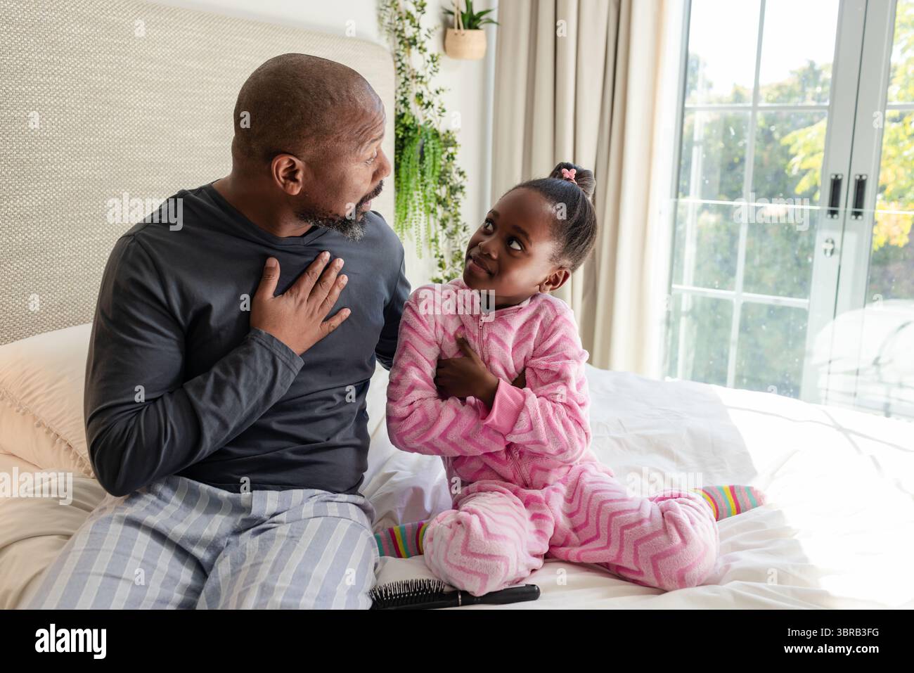 Afroamerikaner Vater und Tochter üben das Atmen auf dem Bett neben Smartphone und Haarbürste Stockfoto
