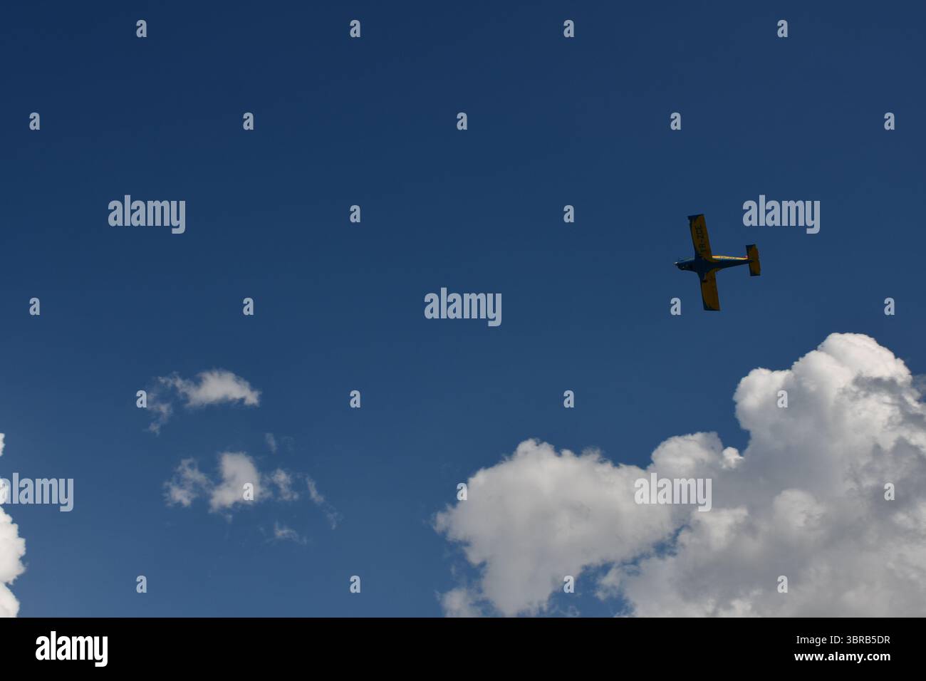 Ein leichtes Kunstflugzeug gleitet während einer Flugshow durch den klaren Sommerhimmel, umgeben von weißen Cumuluswolken und tiefblauer Atmosphäre. Stockfoto