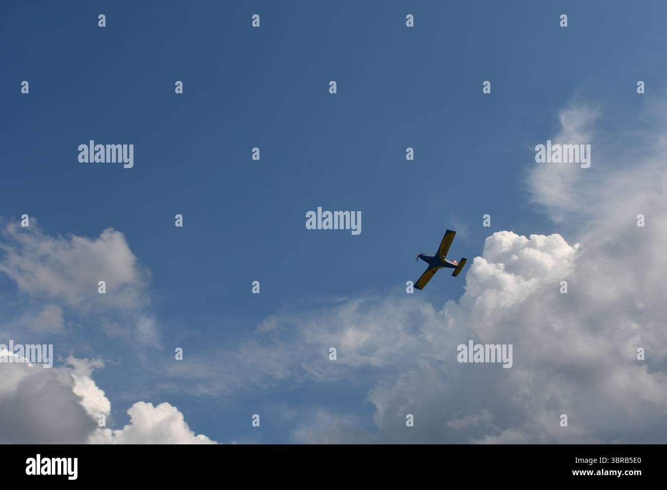 Ein buntes Kunstflugzeug führt während einer Flugshow ein steiles Bankmanöver durch, das sich im Kontrast zum blauen Himmel und den dynamischen Kumuluswolken befindet Stockfoto