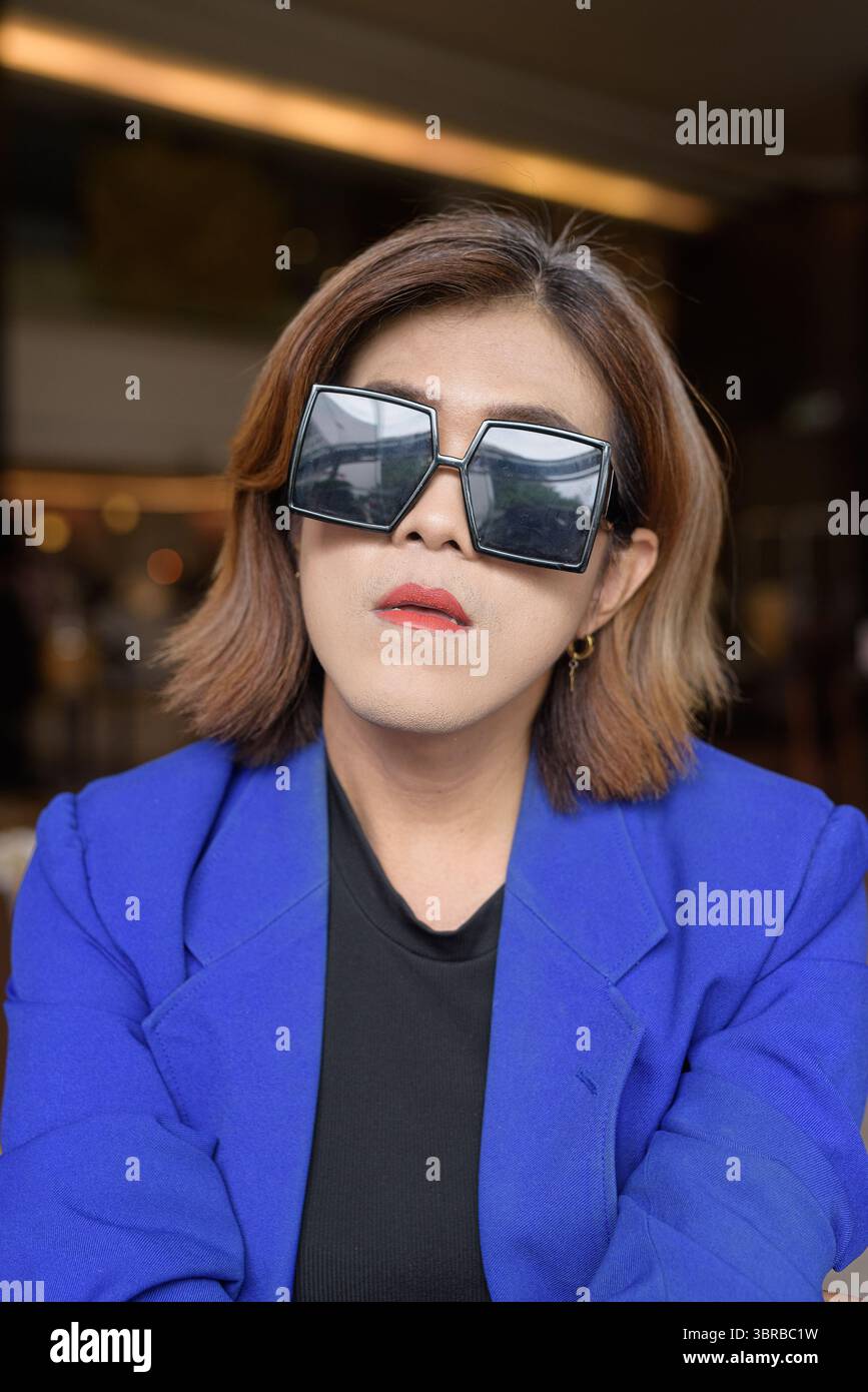 Selbstbewusste asiatische Transgender-Frau im Anzug, die allein im Café sitzt Stockfoto