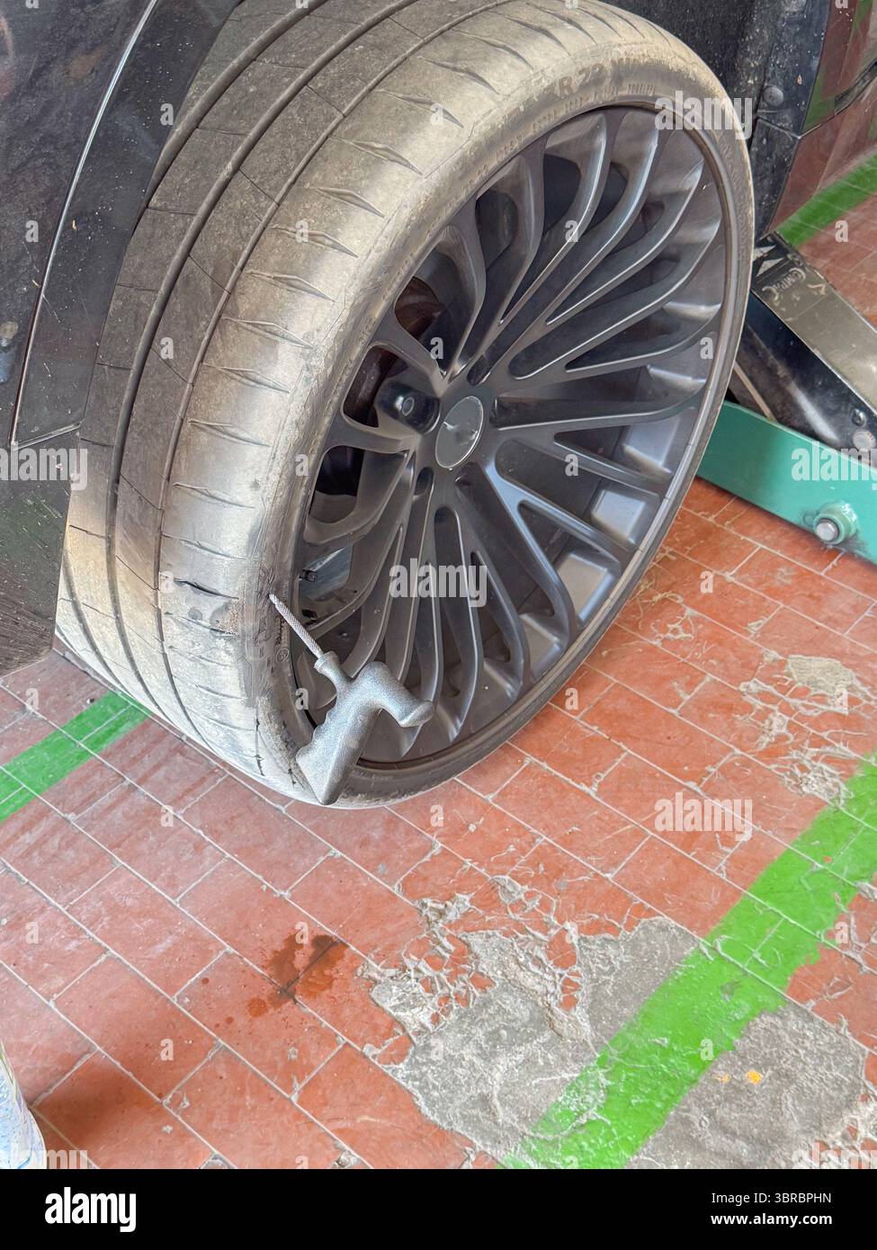 Reifenpannen in einer Garage mit Dichtmittel zur Reparatur einer Reifenpanne. Ein Autorad wird auf einem Wagenheber angehoben, während sich in der Nähe eine Sprühdose für Dichtmittel befindet Stockfoto