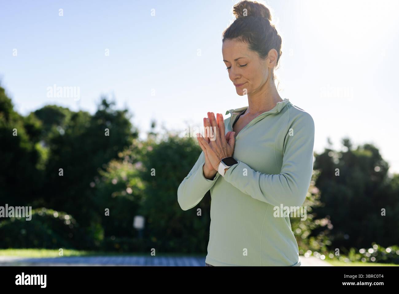 Frau meditiert mit Händen, die auf der Brust auf dem Gartenweg drücken, mit Oberteil, Smartwatch, Kopierraum Stockfoto