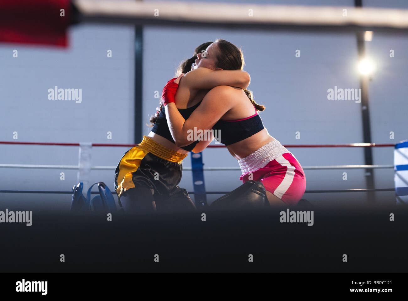 Boxerinnen, die sich im Boxring umarmen, tragen Sport-BHs, Boxshorts und Handschuhe mit Ringseilen Stockfoto