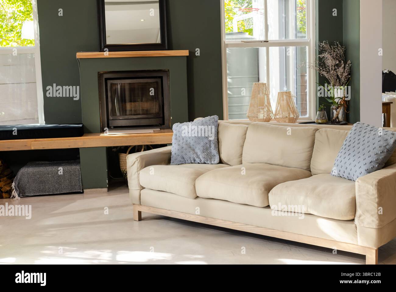 Mit beigefarbenem Sofa mit blauen Kissen gegen grüne Wand und Kamin im Wohnzimmer Stockfoto