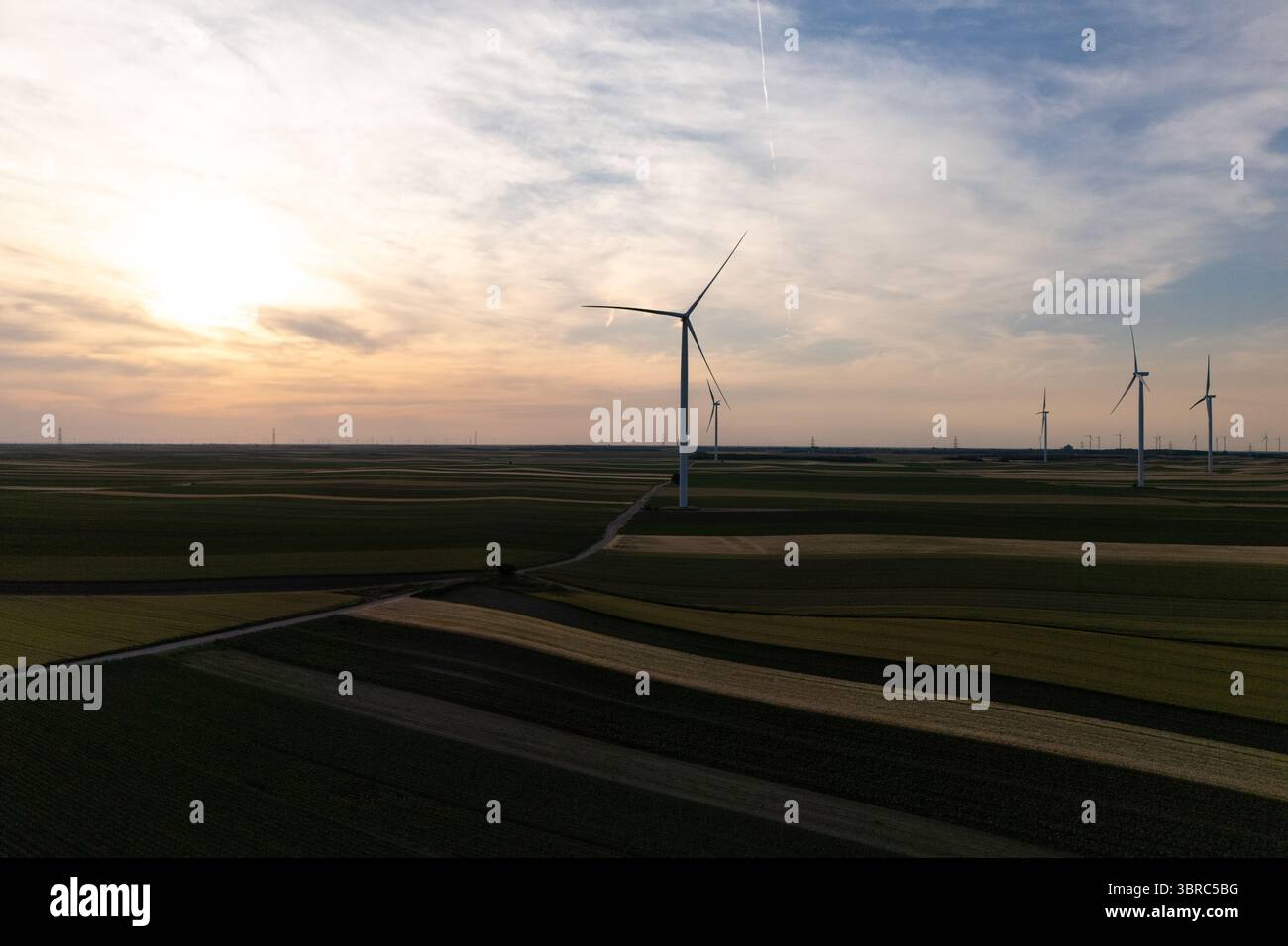 Luftaufnahme von Windturbinen auf einem landwirtschaftlichen Feilchen bei Sonnenuntergang Stockfoto