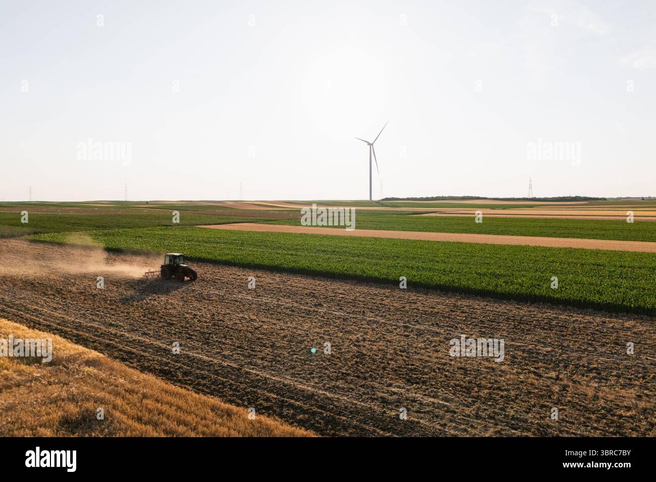 Der landwirtschaftliche Traktor arbeitet auf dem Feld mit Windturbinen. Luftaufnahme. Stockfoto